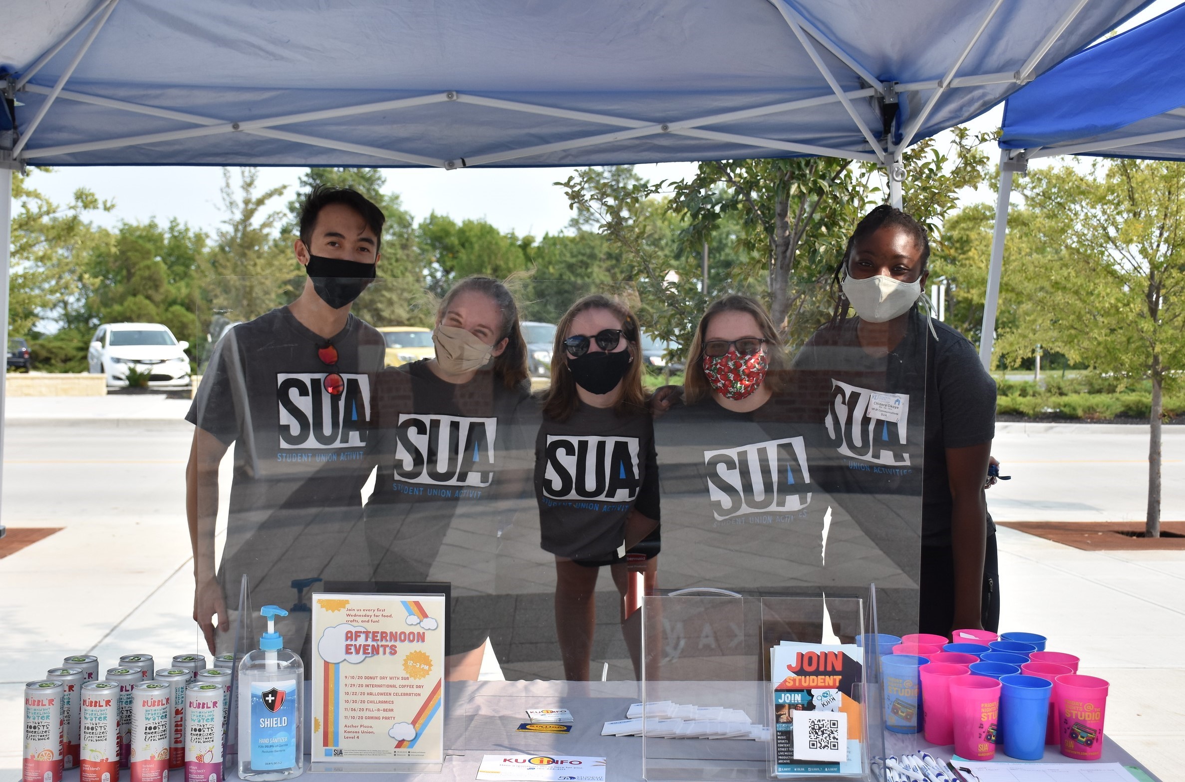 Five students with SUA shirts and masks pose for a photo behind a table